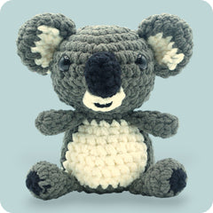A crochet plush toy resembling a koala, with a gray body, white belly, and black ears.