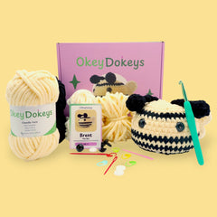 A crochet bee kit by OkeyDokey displayed with yarn, a crochet hook, safety eyes, stuffing needle, stitch markers, and a partially completed plush bee.