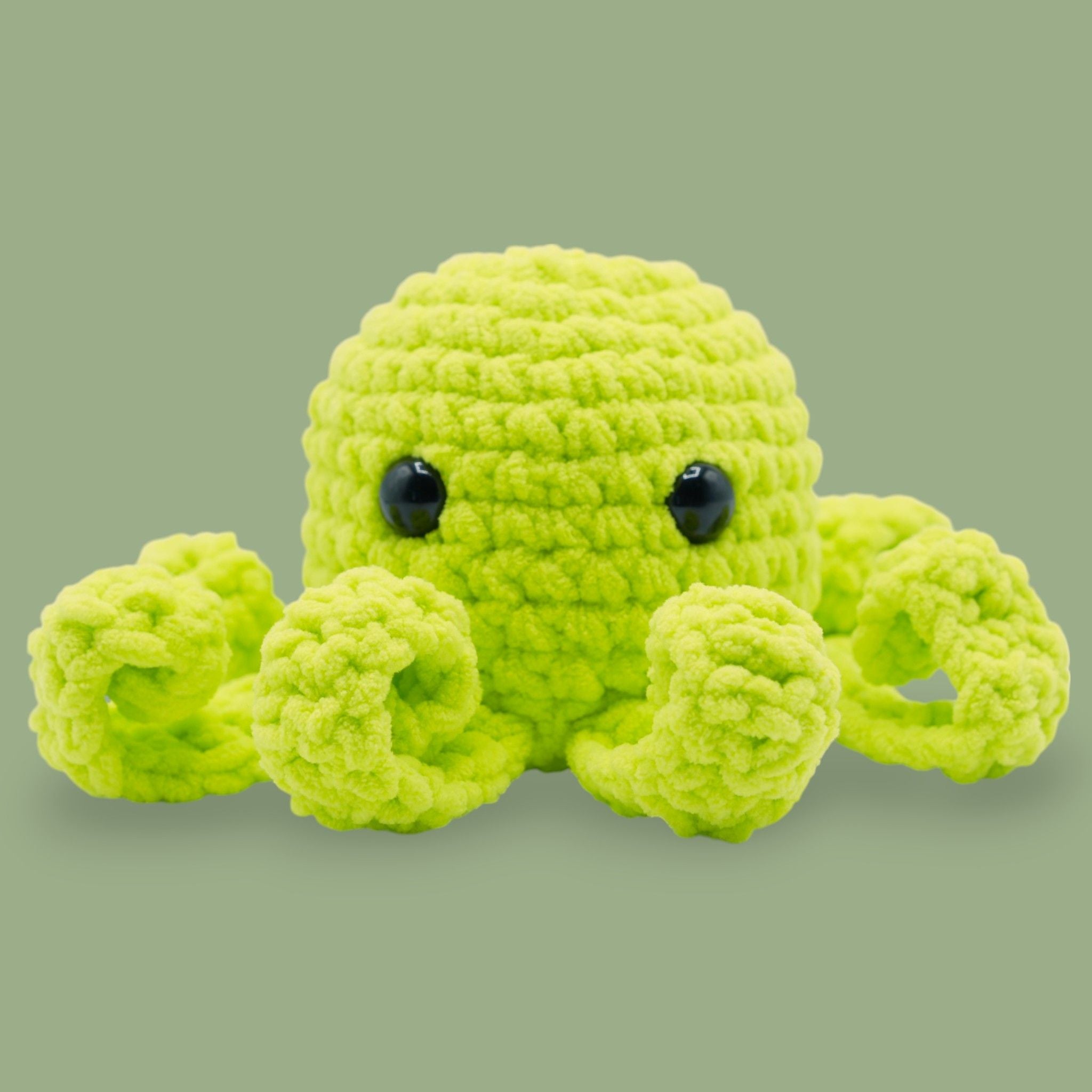 A crochet octopus kit by OkeyDokey, including purple chenille yarn, a crochet hook, safety eyes, stuffing needle, stitch markers, and a pattern booklet, alongside the completed purple octopus plush.