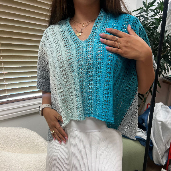 Person wearing a blue and gray crocheted shawl in a casual indoor setting.