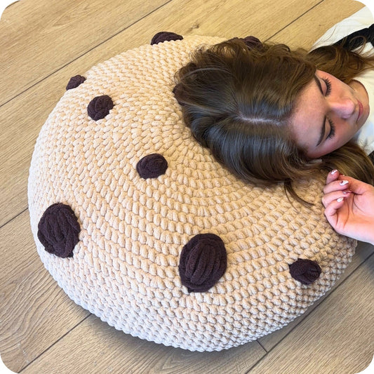 Person lying on a round pillow with brown spots on a wooden floor