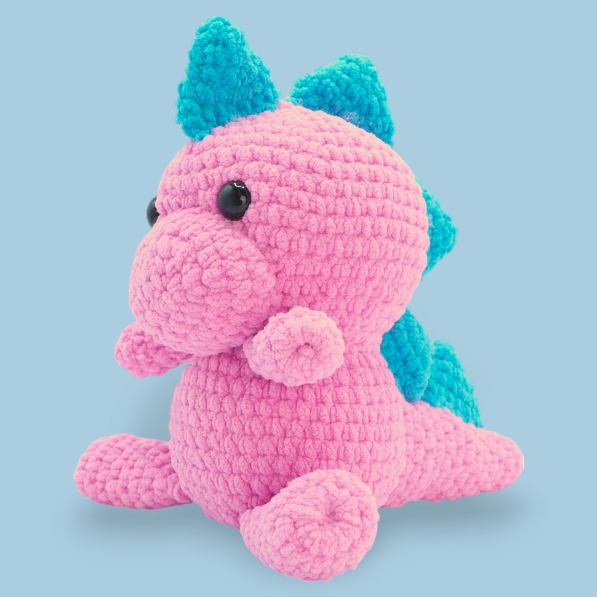 A crochet dinosaur kit in pink and blue colors, designed to look like a plush toy.