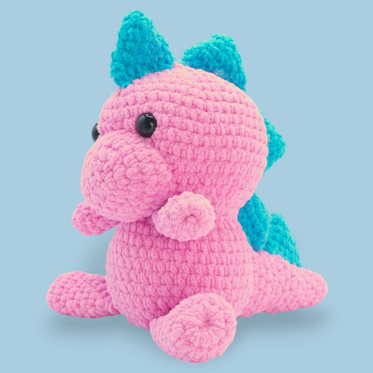 A crochet dinosaur kit in pink and blue colors, designed to look like a plush toy.