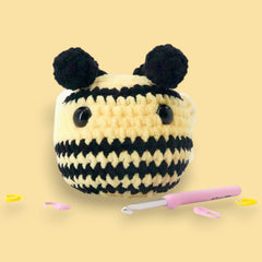 crochet bumble bee with wings decorated with stitch markers and crochet hook all around the base