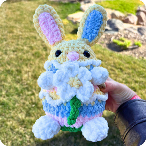 Crocheted bunny holding flowers with a grassy background