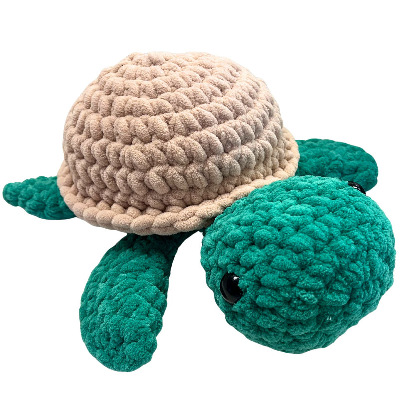 Crocheted turtle toy with beige shell and green body on a white background