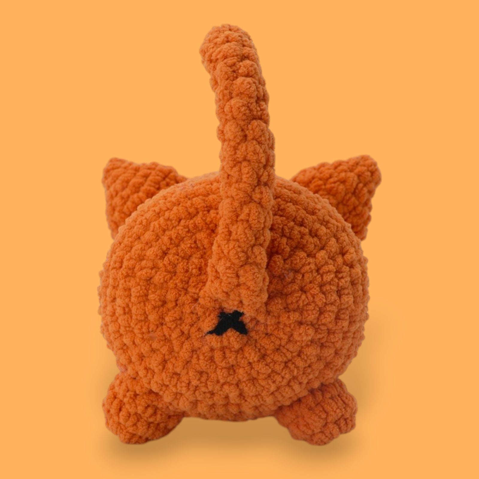 A crochet cat kit by OkeyDokeys, featuring a plush cat toy in orange, pink, and white colors, along with chenille yarn, a crochet hook, safety eyes, stuffing needle, and stitch markers.