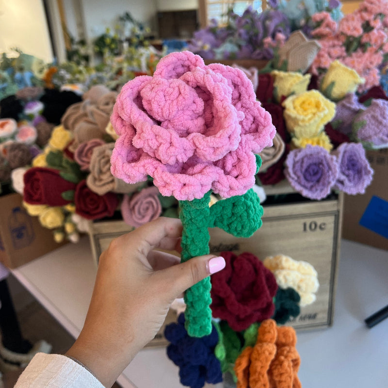 Hand holding a pink crocheted flower with more flowers in the background