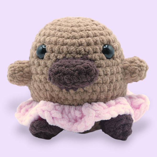 Crocheted animal plush toy with a pink skirt on a light purple background