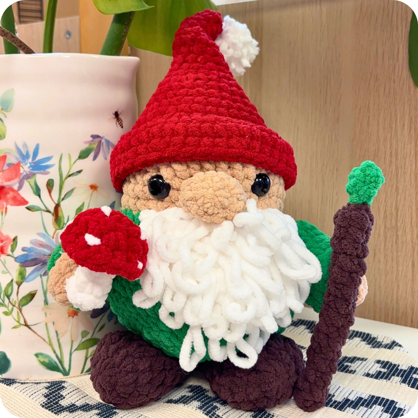 crocheted gnome with a red hat and white beard sitting on a surface.