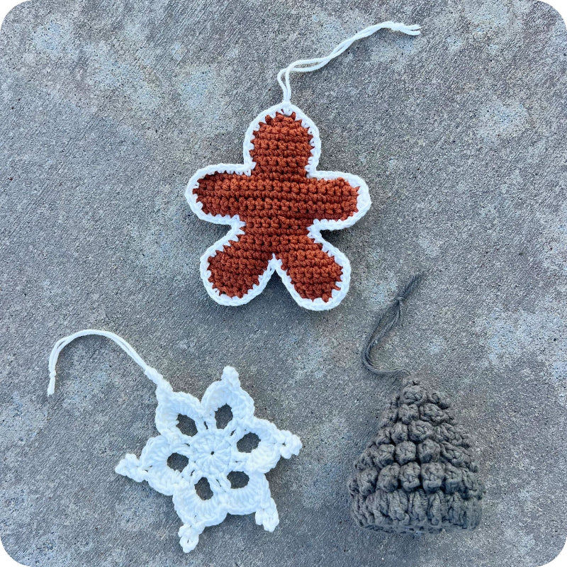 Three crocheted ornaments on a textured surface: a gingerbread man, a snowflake, and a tree.
